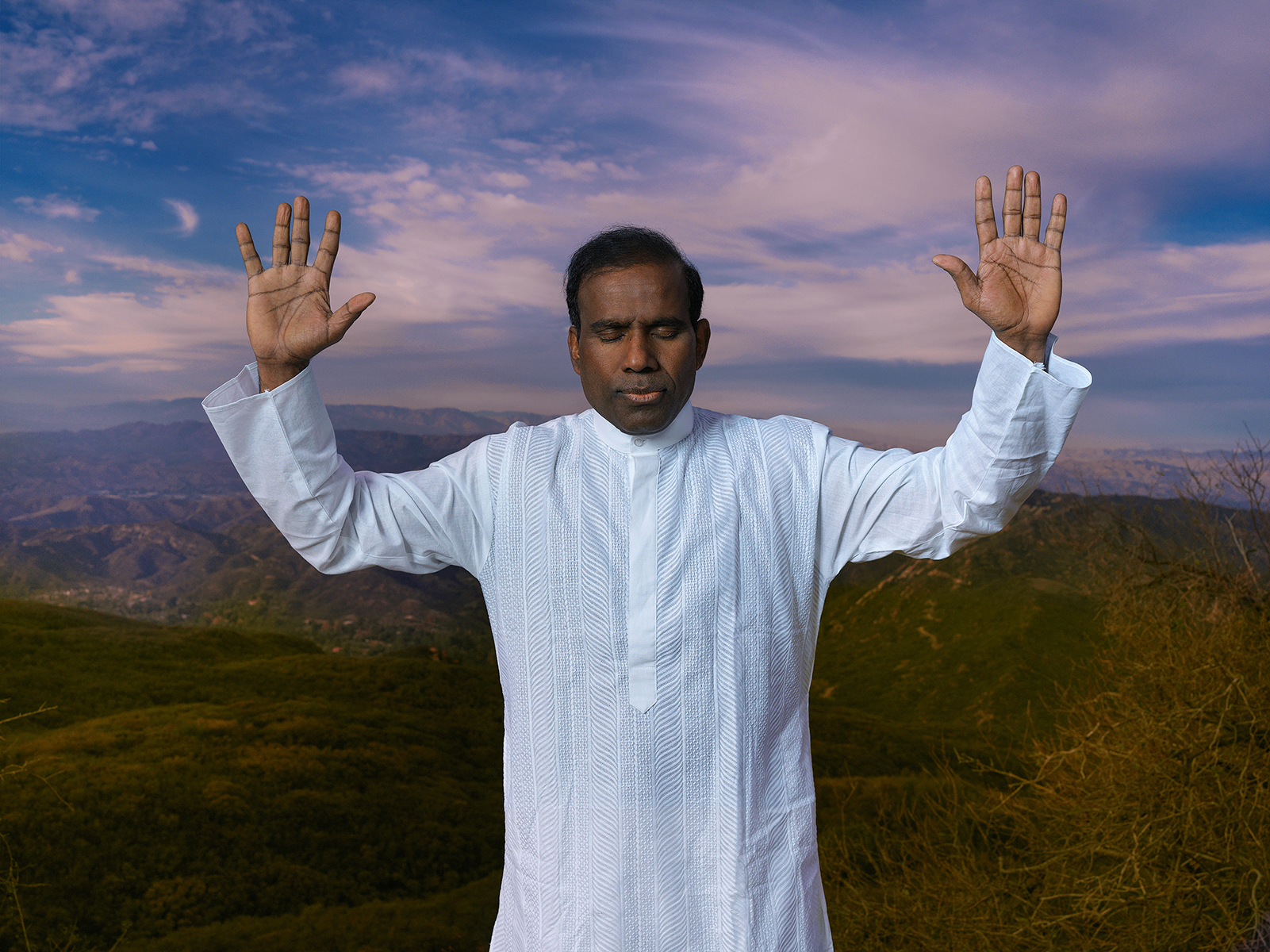 Dr. K.A. Paul in prayer with raised hands on a mountaintop at dusk