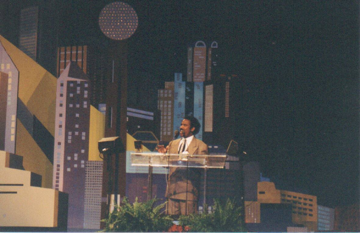 Dr. K.A. Paul preaching from a podium before a stylized cityscape backdrop